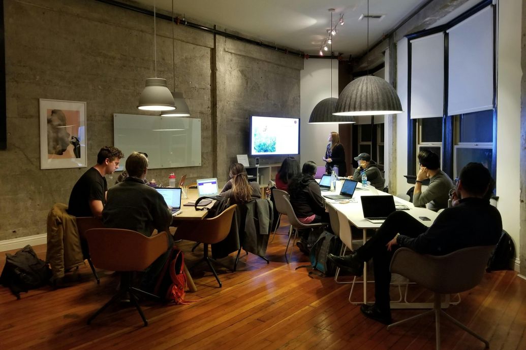 Diverse team collaborating in a modern office setting with laptops and presentation screen.